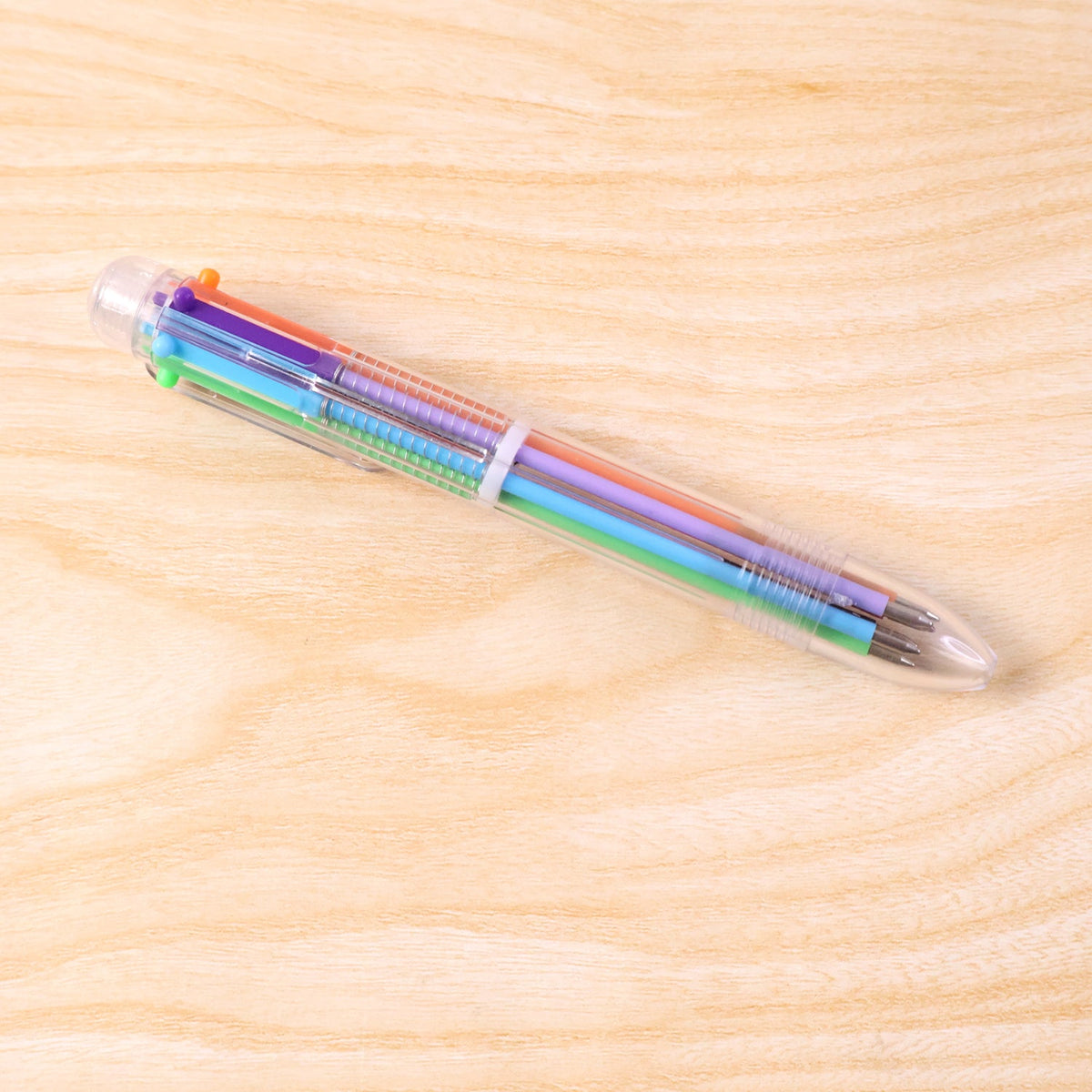 A clear 6-in-1 multicolor ballpoint pen with various ink colors is centered on a light wooden surface.