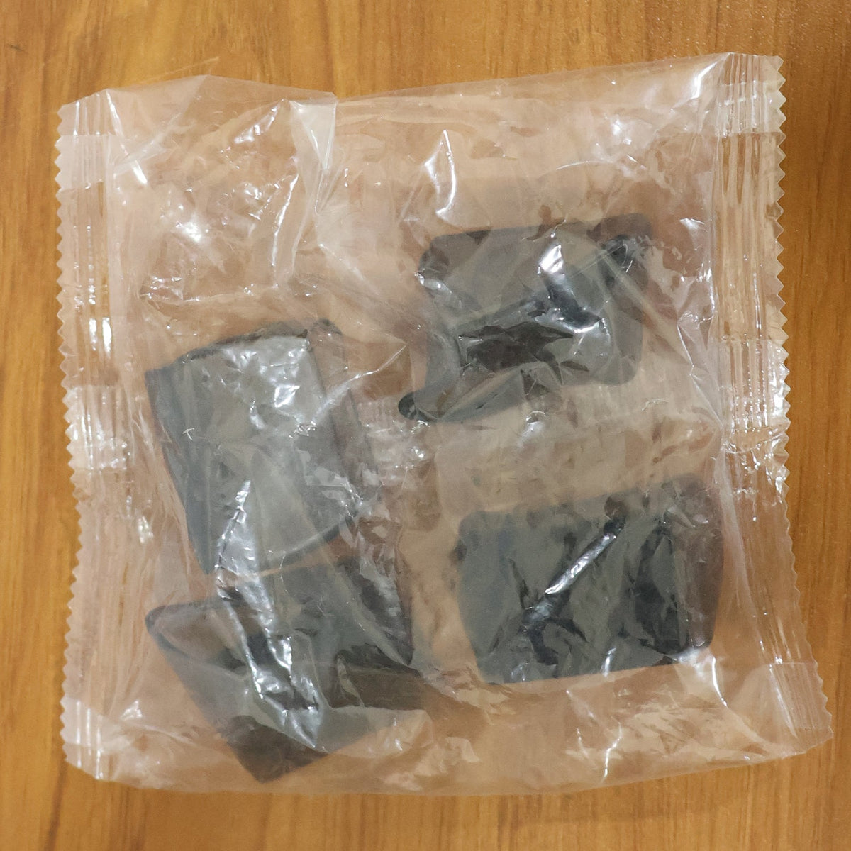 Four dark grey silicone furniture leg caps are sealed in clear plastic packaging on a wooden surface.