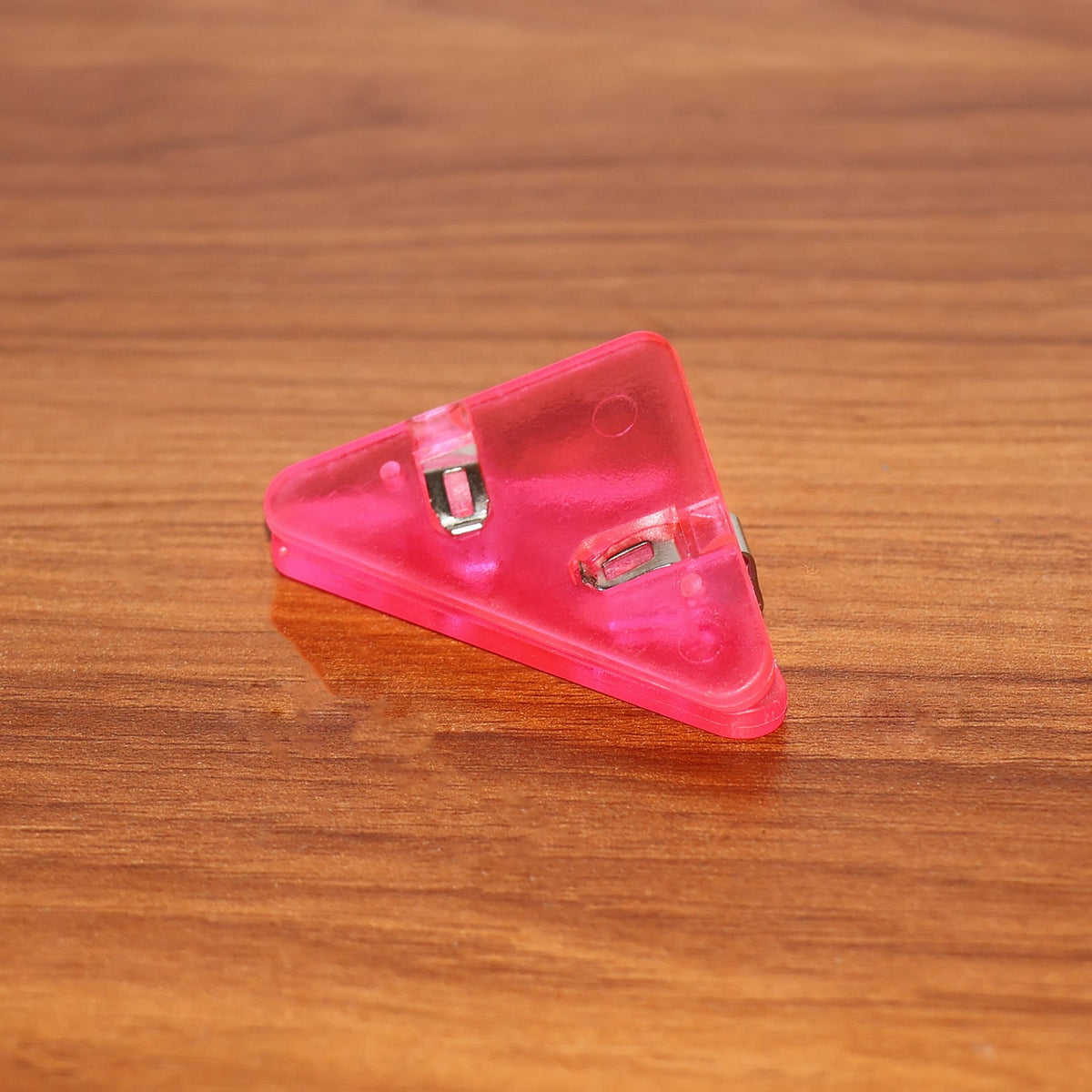 A pink plastic triangle corner clip on a wooden desk surface.