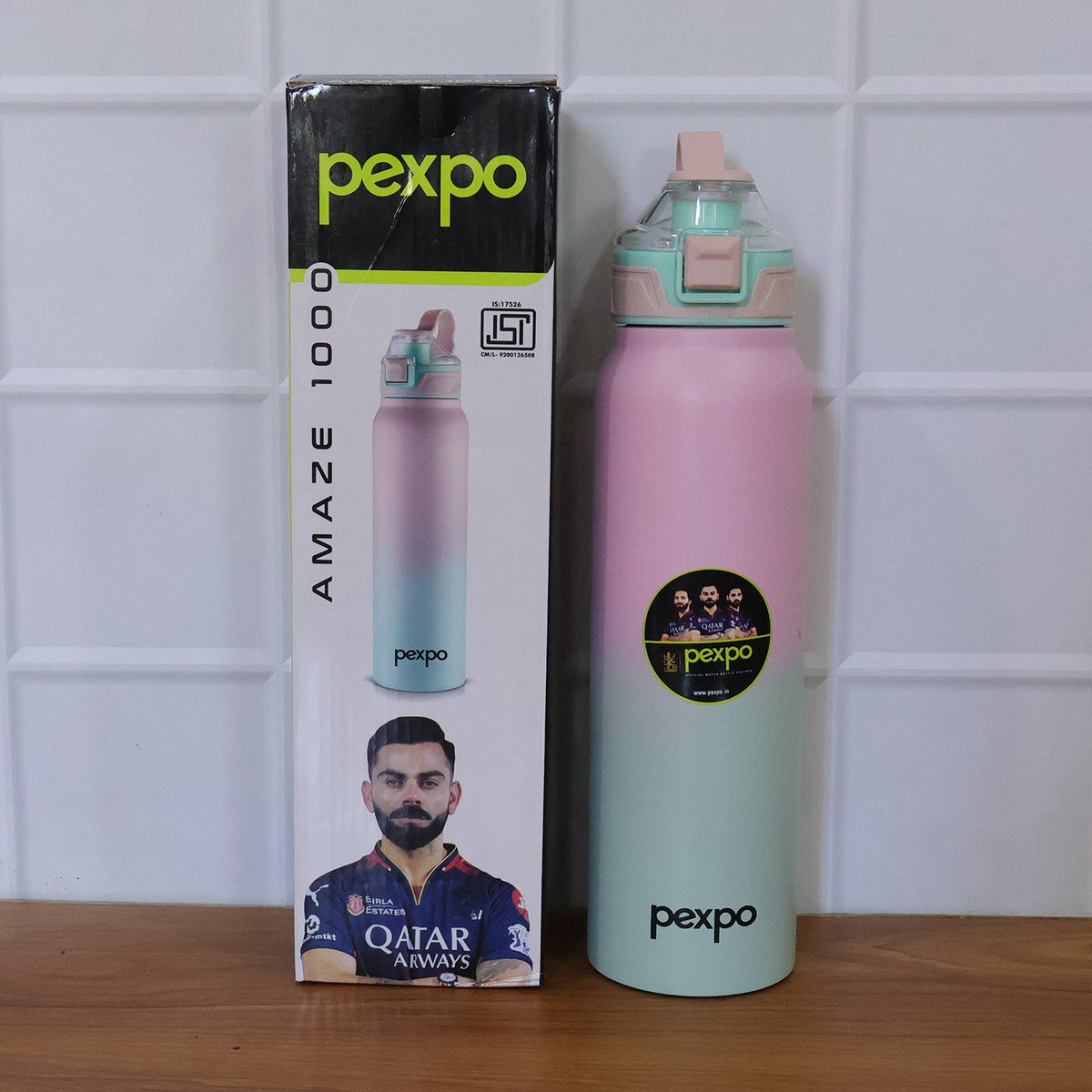 A pink and green gradient water bottle with a woman drinking from it in an inset. The bottle is on a counter with weights in