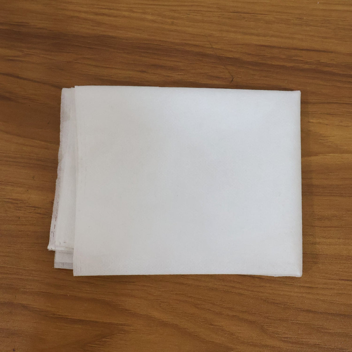 A stack of folded white non-woven bags resting on a light brown wooden surface.