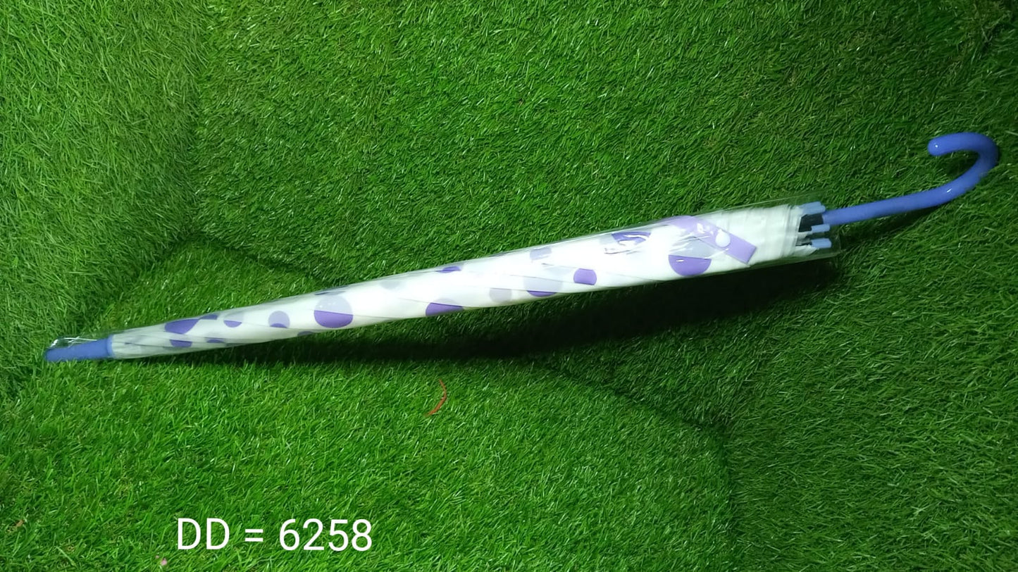 A closed white umbrella with purple geometric shapes and a blue handle rests horizontally on a green artificial grass