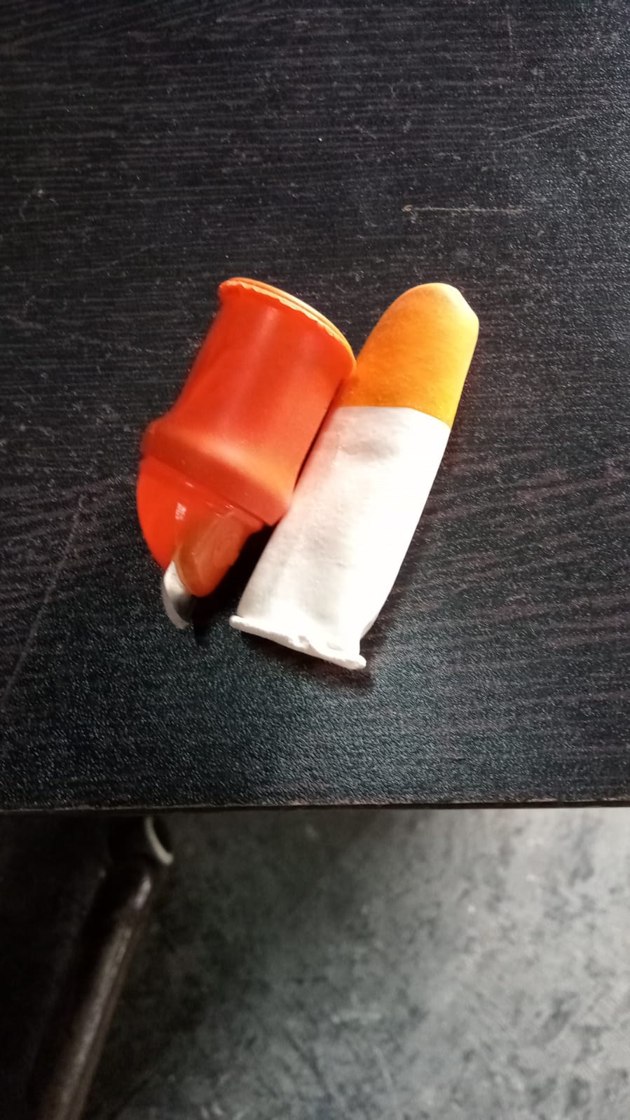 An orange thumb cutter with a blade and a white and orange finger protector lie on a dark, textured surface.