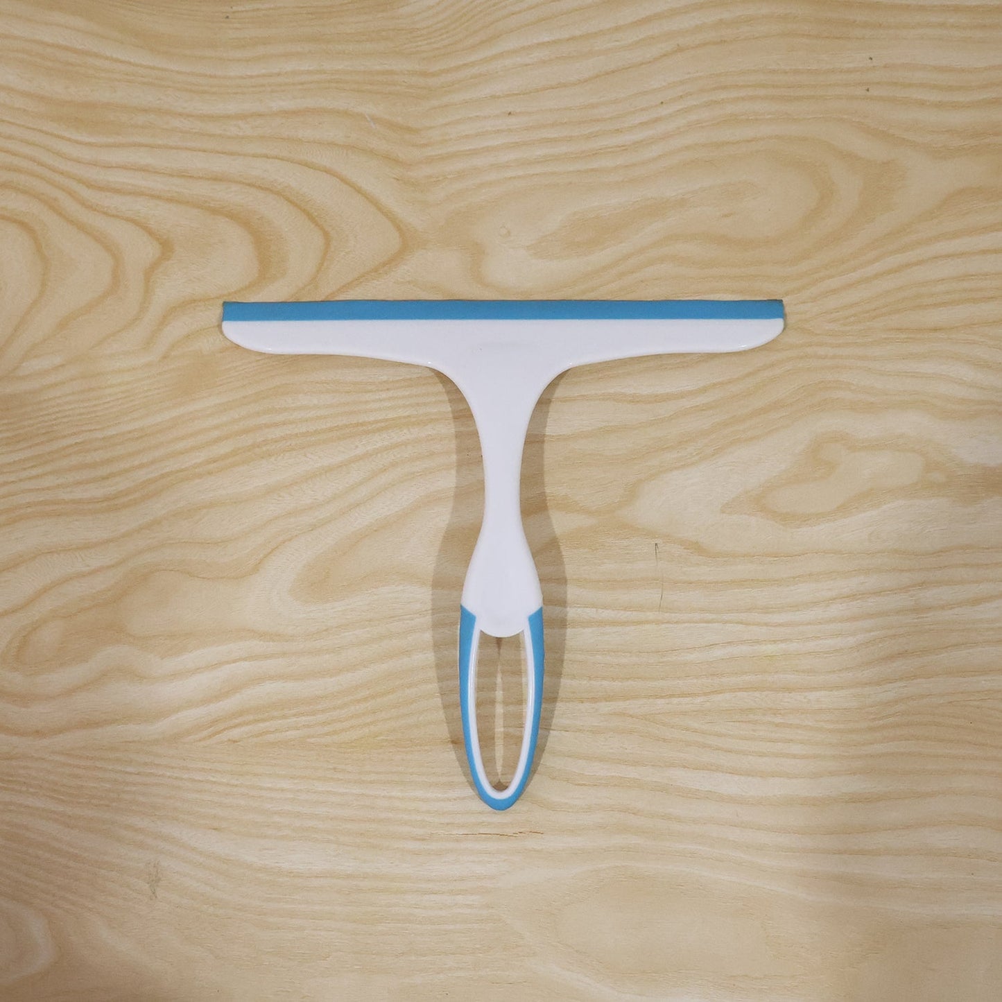 A white and blue squeegee lies flat on a light wooden surface with a visible grain.