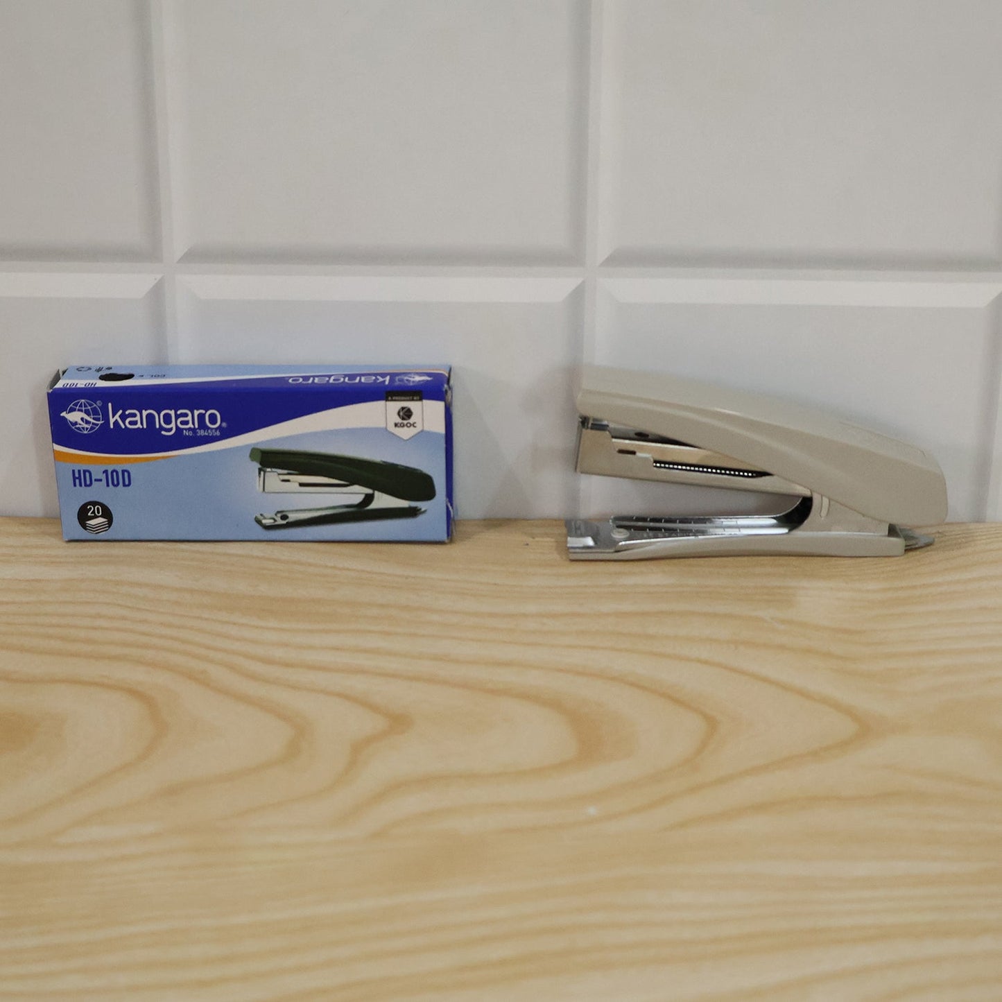 A beige and silver stapler sits next to its blue and white Kangaro brand box on a wooden surface.