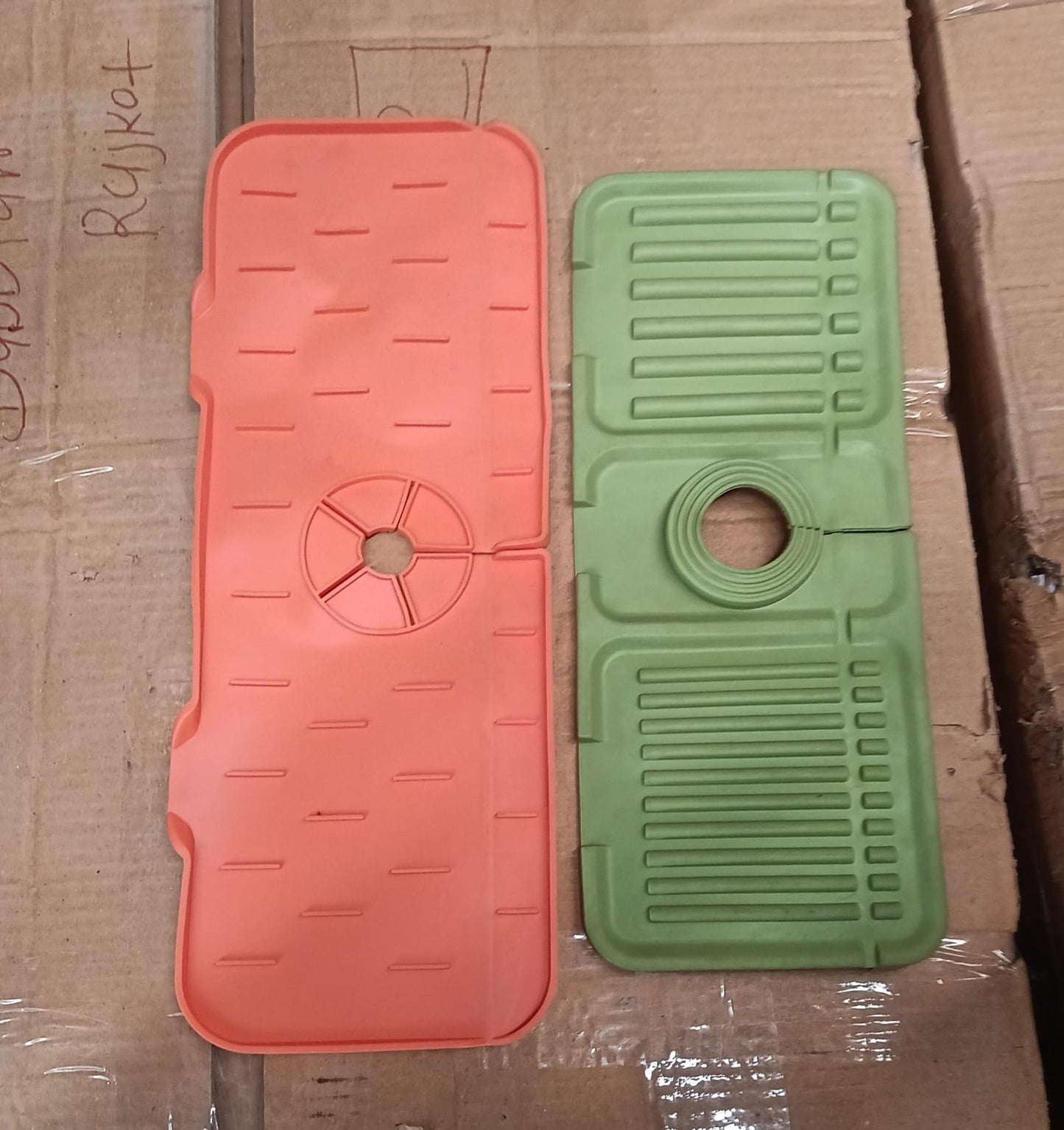 One orange and one green silicone faucet splash guard lying on a cardboard surface.
