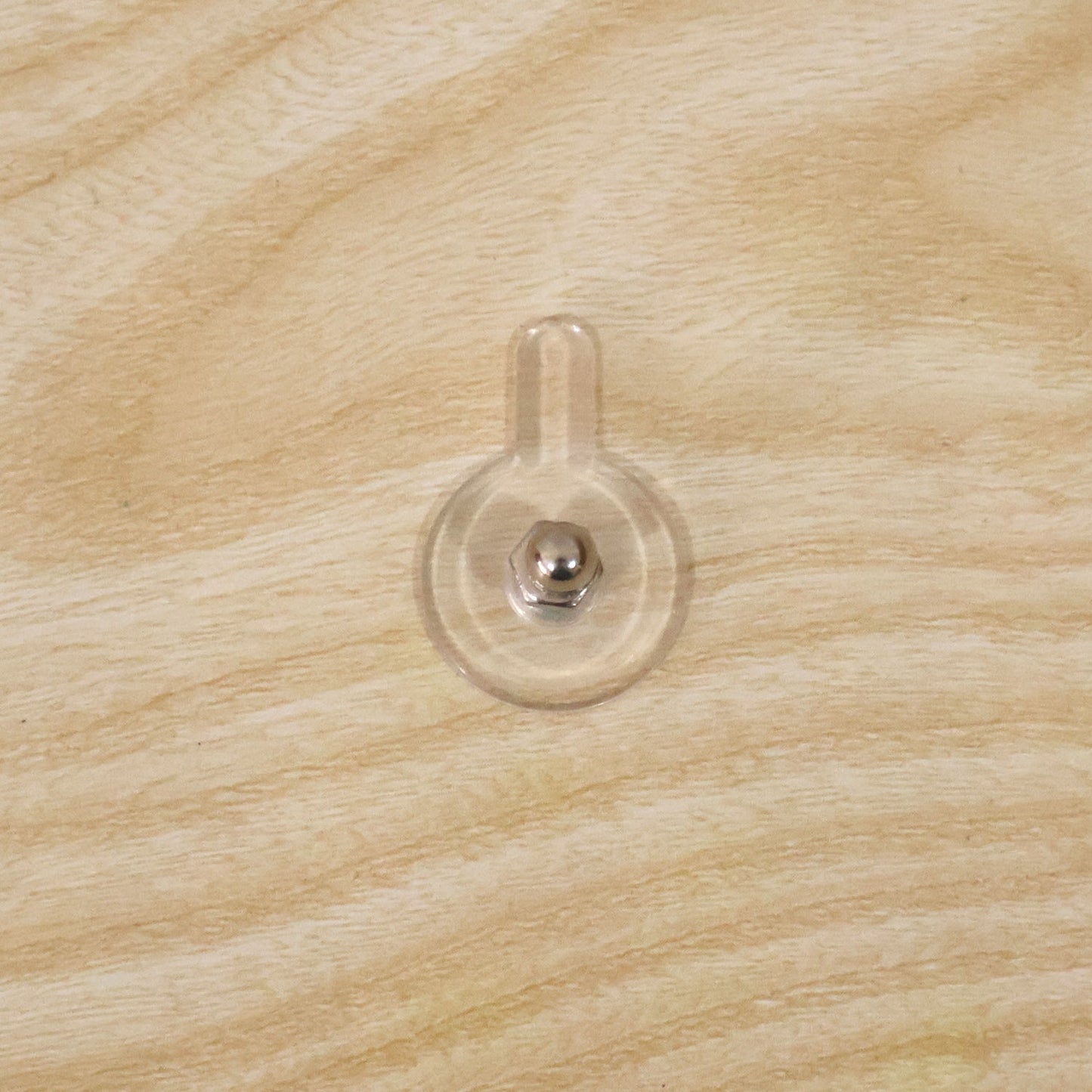 A clear self-adhesive wall hook with a silver knob is attached to a light-colored wooden surface.