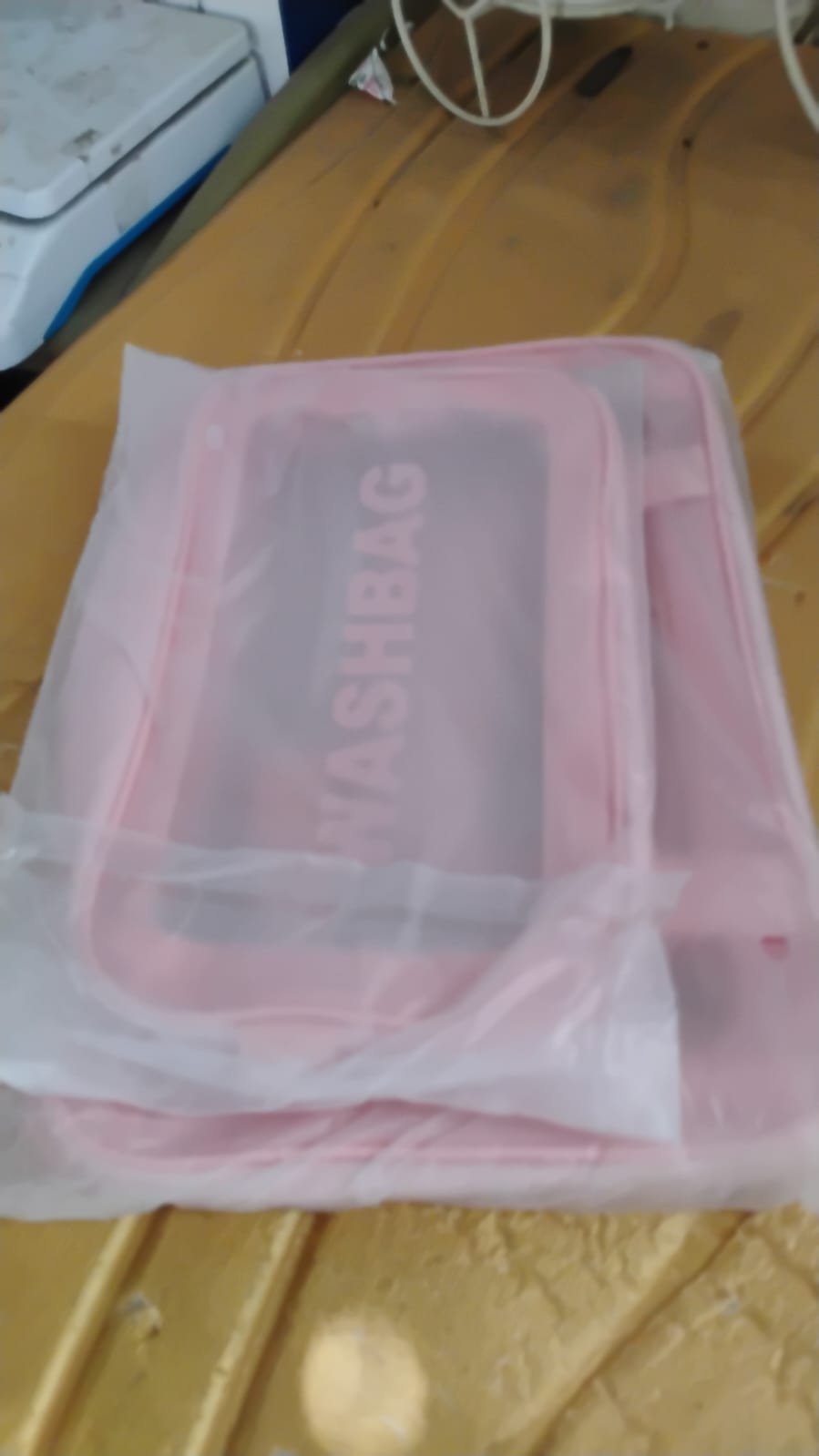 Two pink waterproof travel bags with clear panels are shown inside a plastic packaging bag on a yellow surface.