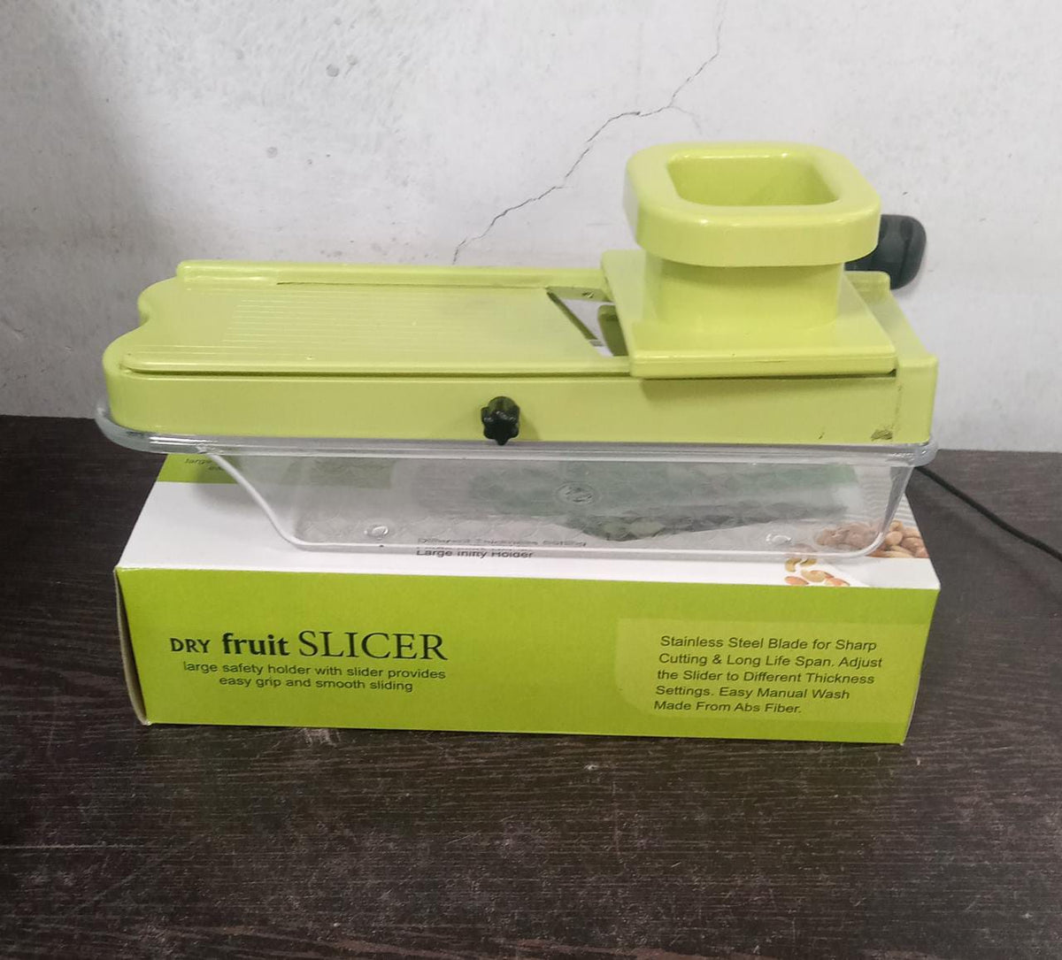 A green plastic dry fruit slicer with a clear container sits on its green and white product box.