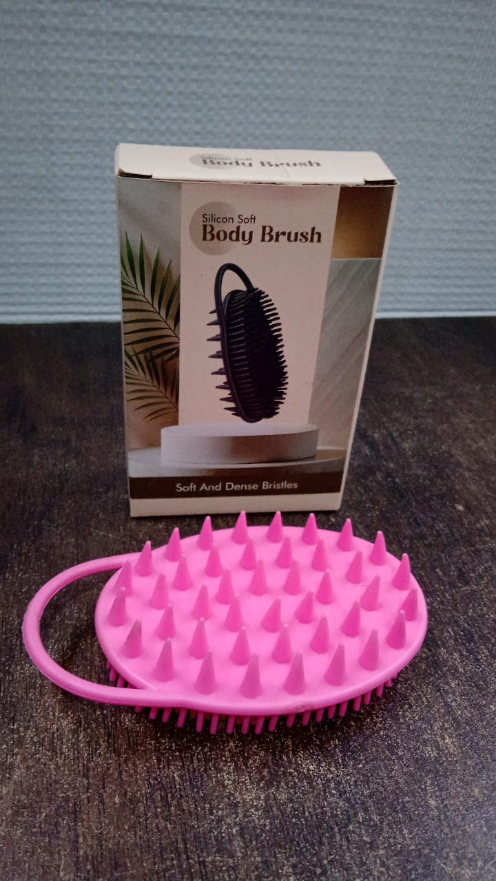 A pink silicone body brush with spiky bristles lies on a dark wooden surface in front of its product packaging box.
