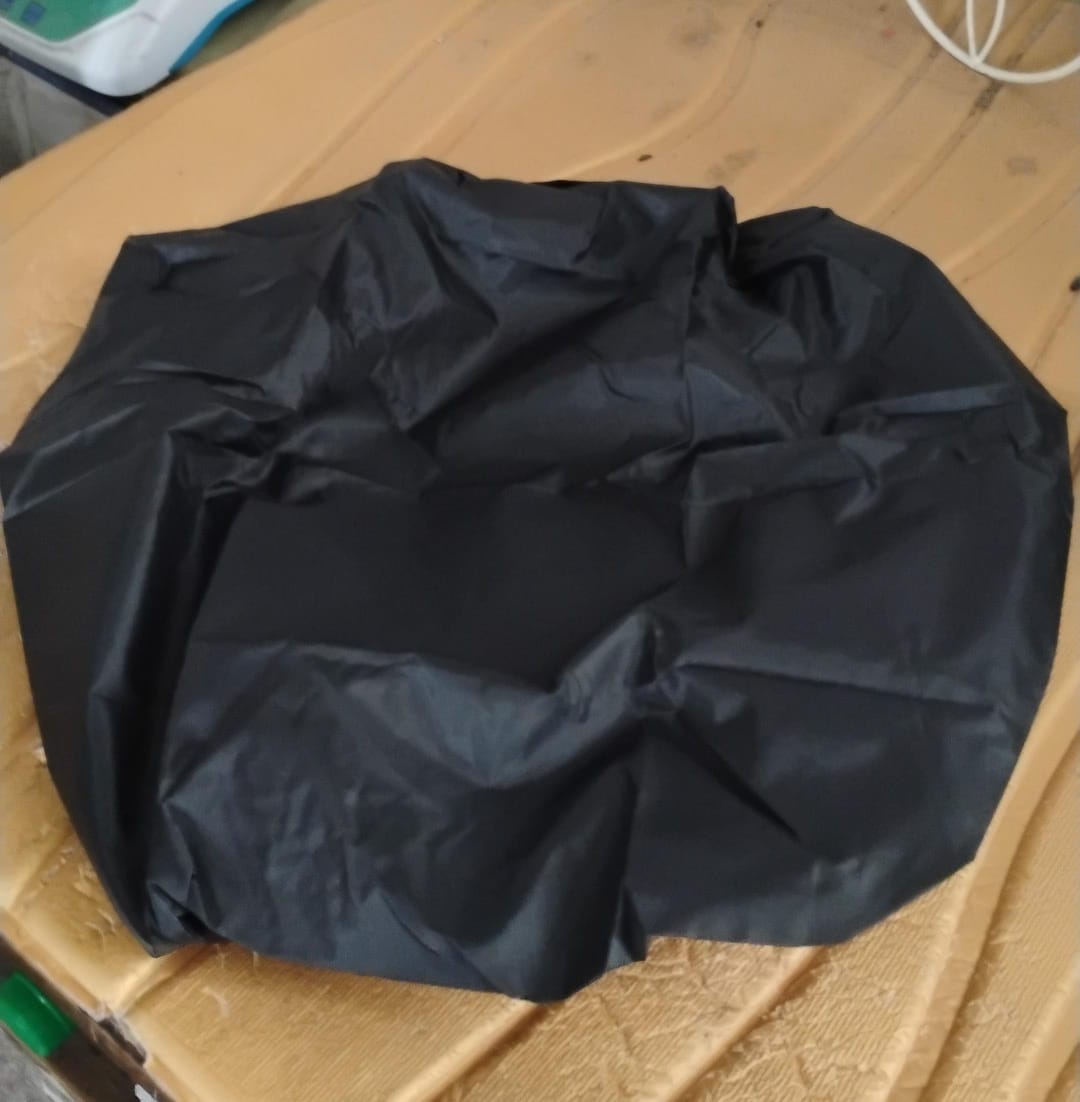 Black waterproof backpack rain cover lying flat on a textured brown surface.