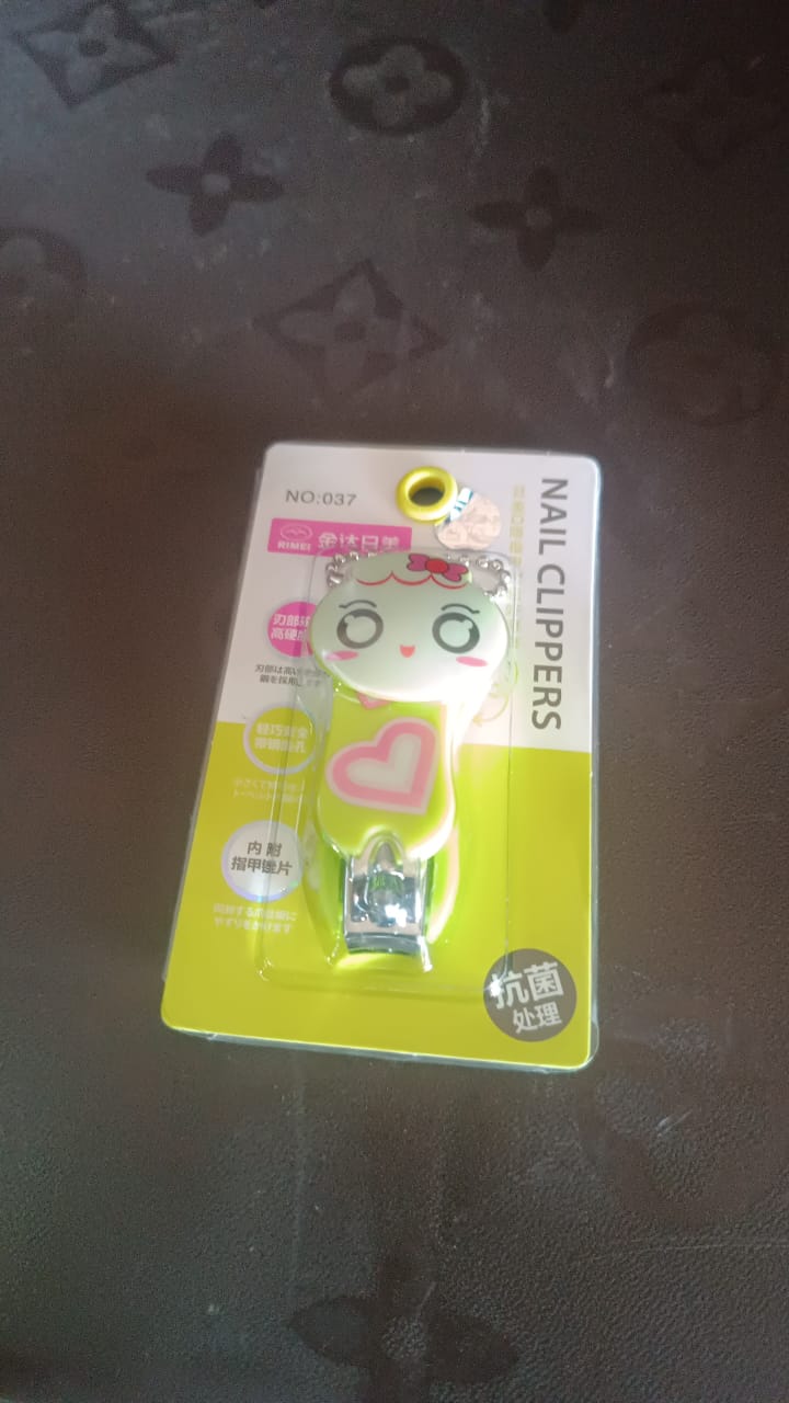 A green and white cartoon character nail clipper with a pink heart, in its clear plastic packaging with