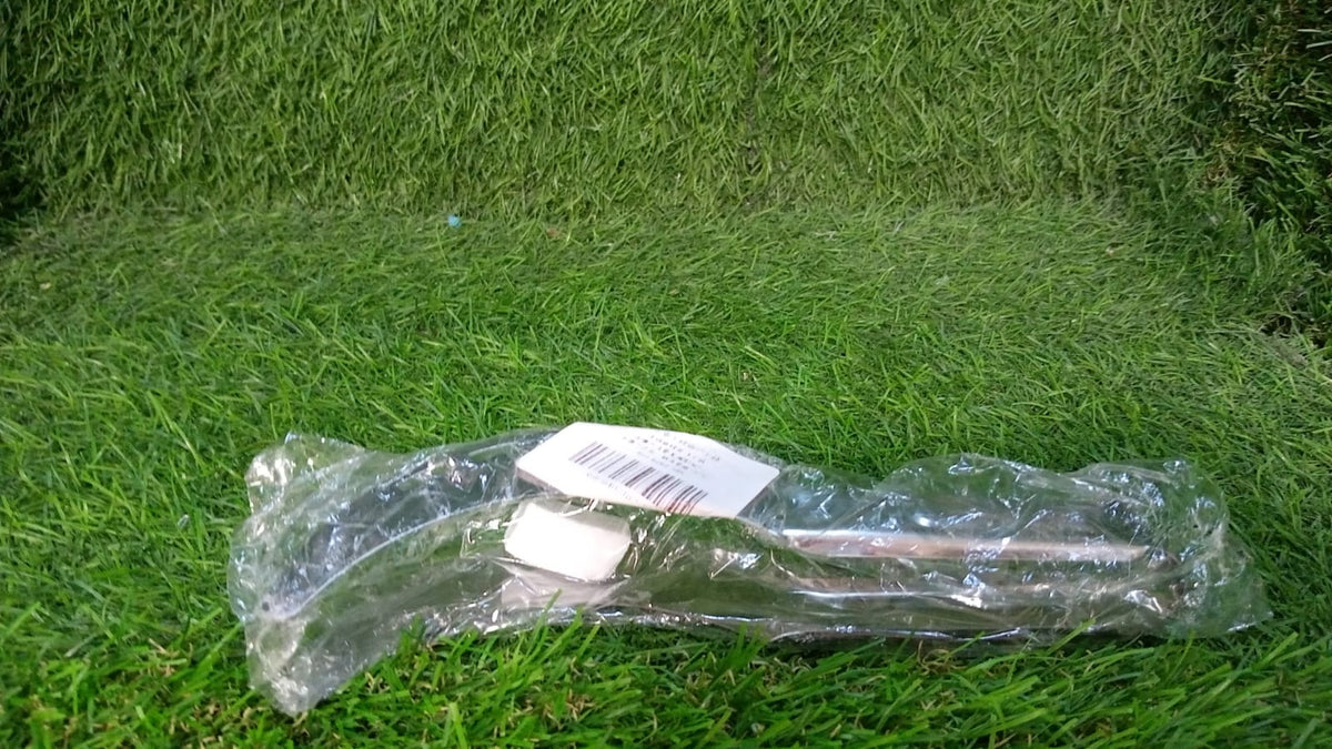 A clear plastic-wrapped stainless steel watermelon slicer with a white label lies on a vibrant green grassy surface.