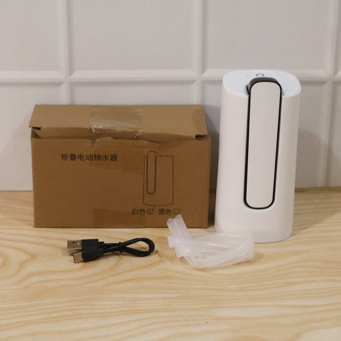 A white and gray foldable water dispenser, a brown cardboard box, a USB charging cable, and a clear silicone hose are
