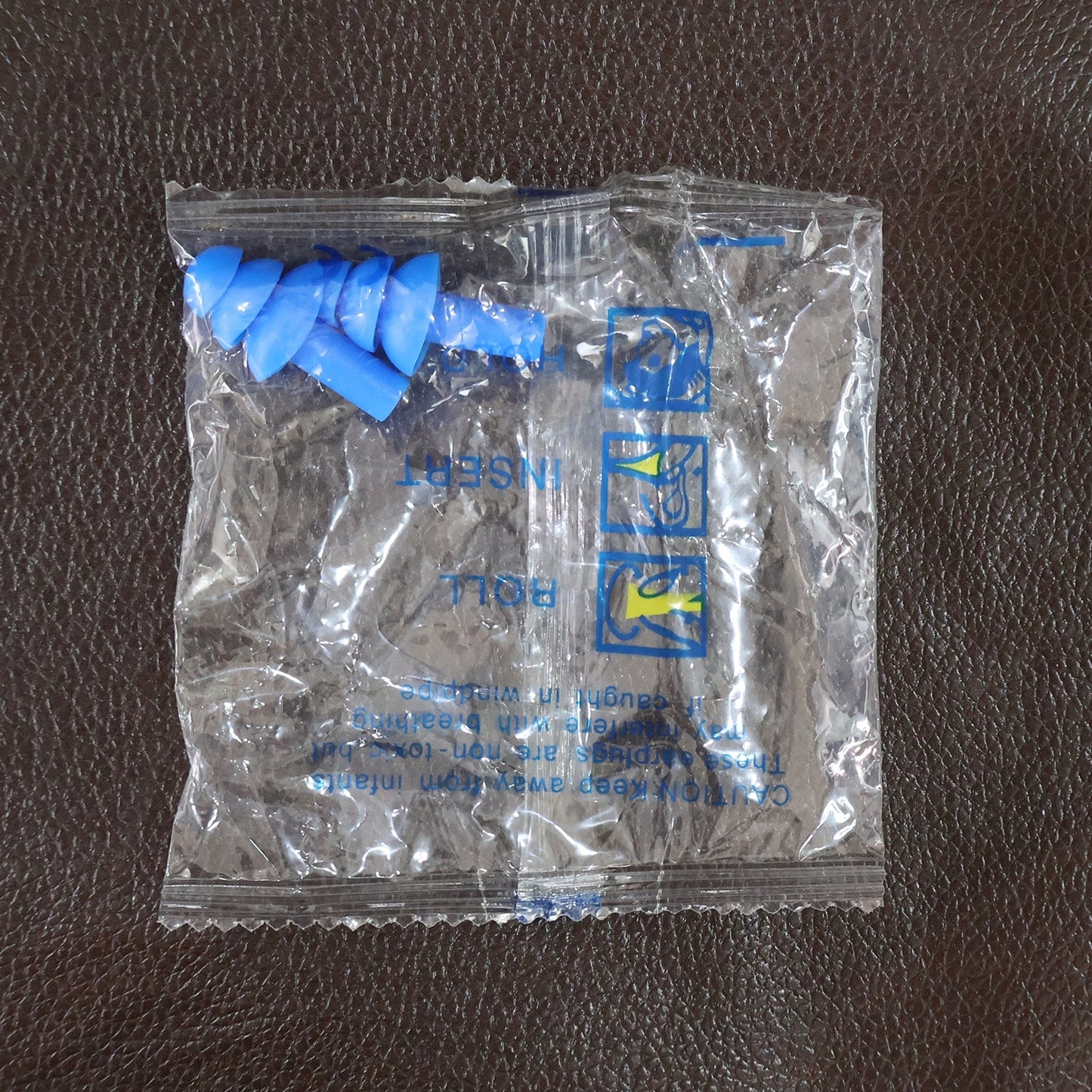 A clear plastic package containing two blue silicone earplugs and instructions is shown on a dark brown surface.