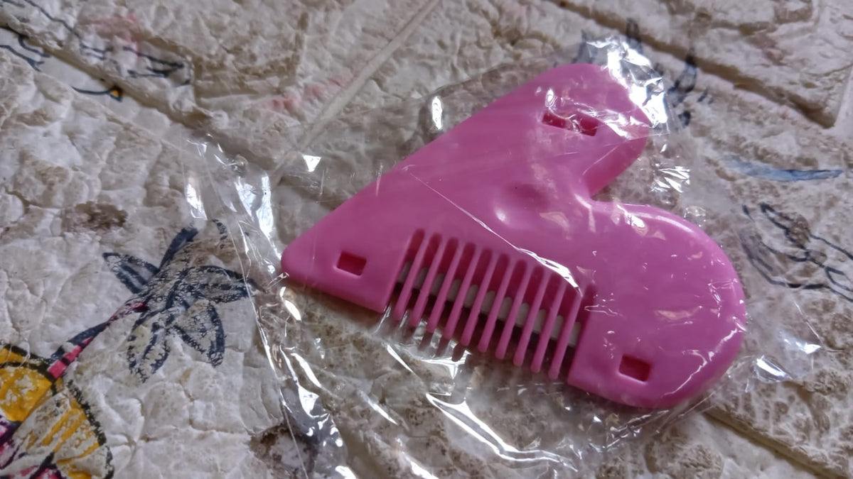 A pink heart-shaped hair thinning razor comb is sealed in clear plastic packaging on a patterned blanket.