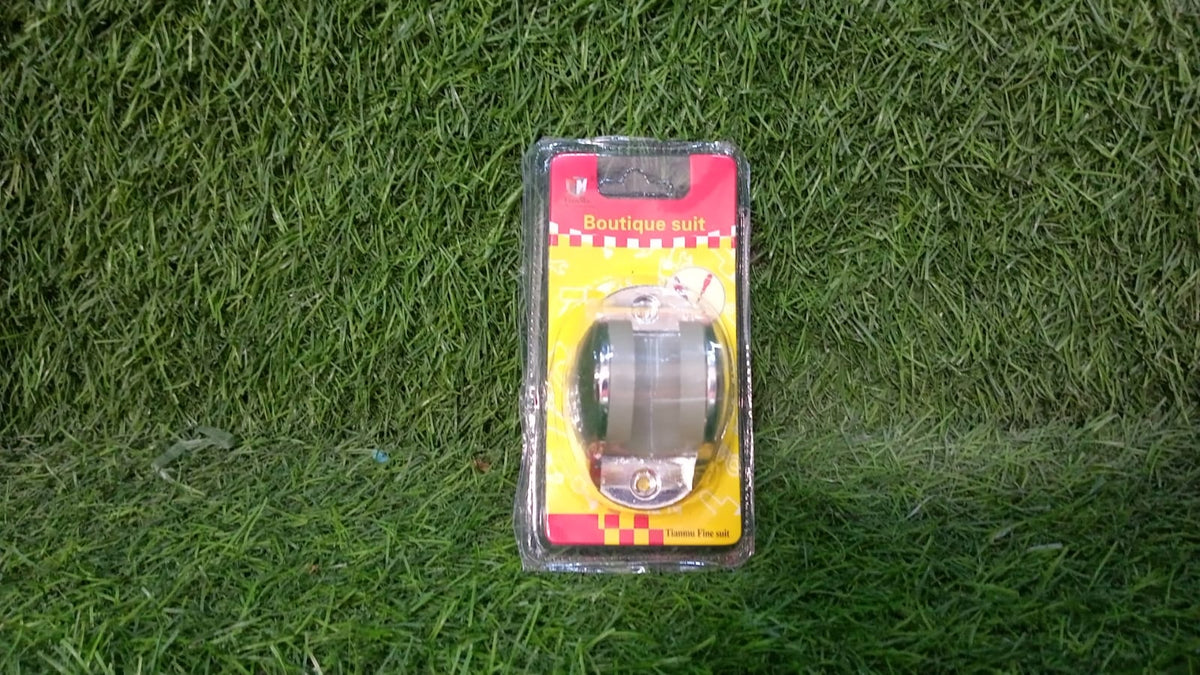 A chrome shower head holder in clear plastic packaging with a red and yellow label rests on a vibrant green grassy surface.