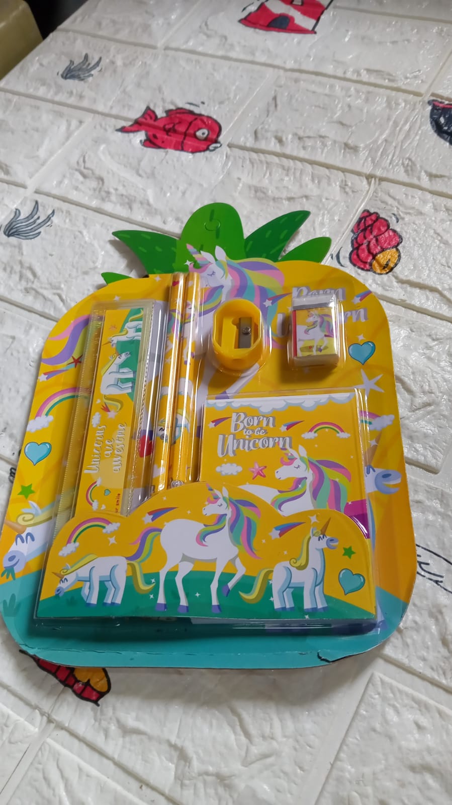 A yellow unicorn-themed stationery set in pineapple packaging, including pencils, a ruler, sharpener, eraser, and notebook
