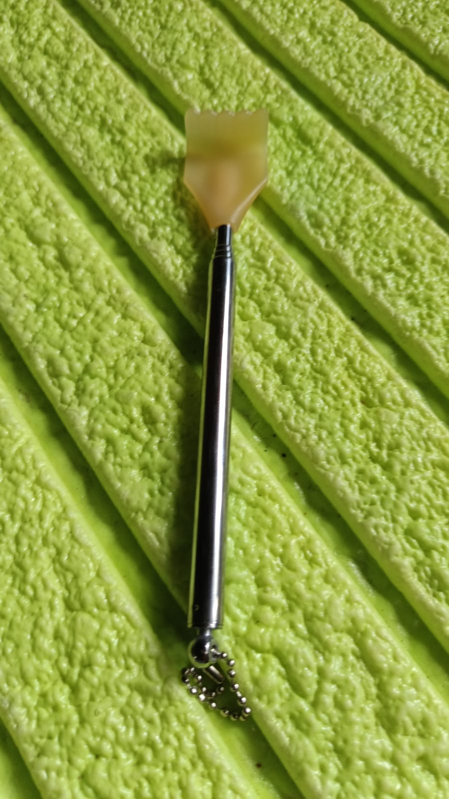 A silver telescoping back scratcher with a yellow hand-shaped head resting on a textured green surface.