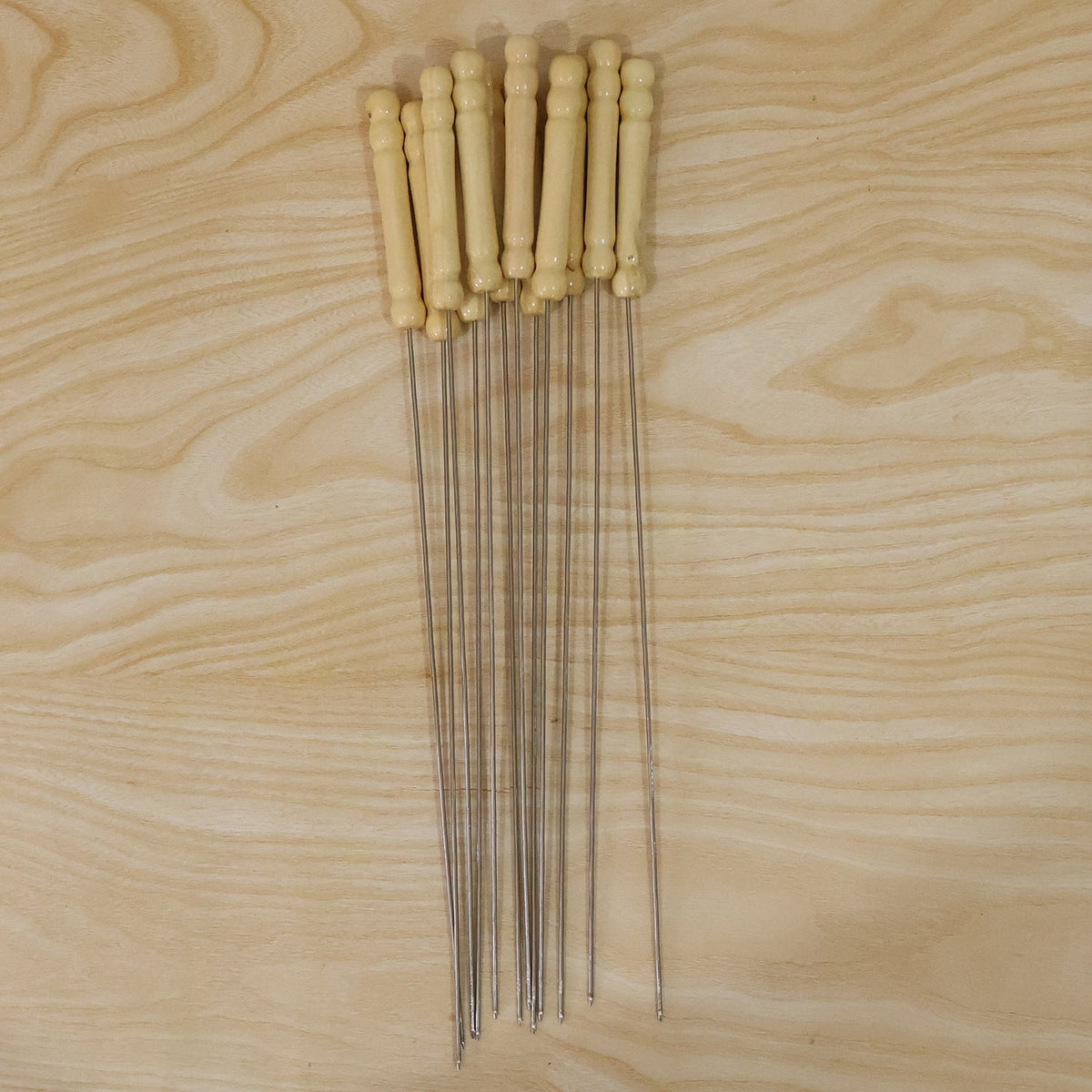 A bundle of stainless steel skewers with light wooden handles lying on a light wooden surface.