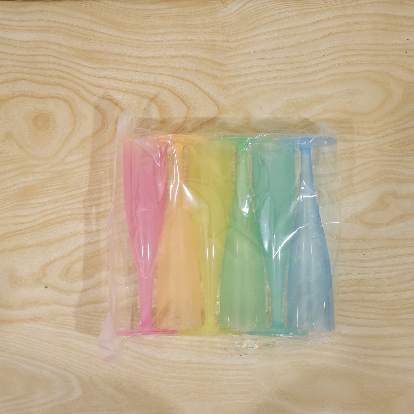 Six colorful plastic champagne flutes in pink, yellow, orange, green, and blue, sealed in clear plastic packaging.
