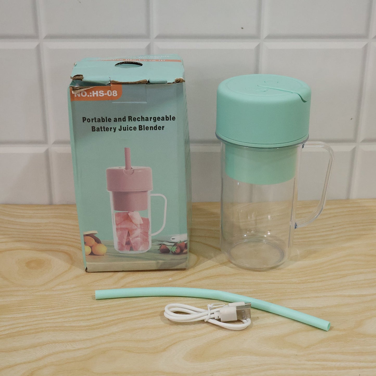 A mint green blender bottle, a matching straw, and a white USB cable are displayed next to its product box on a wooden
