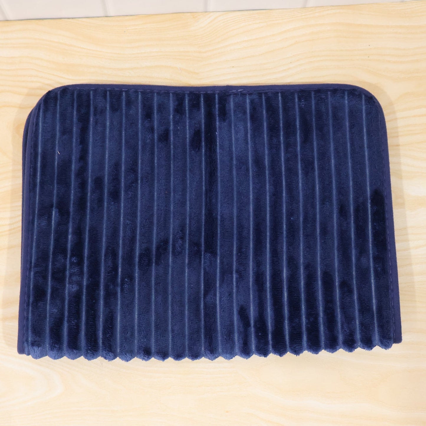 A navy blue ribbed memory foam bath mat is folded in half, resting on a light wooden surface.