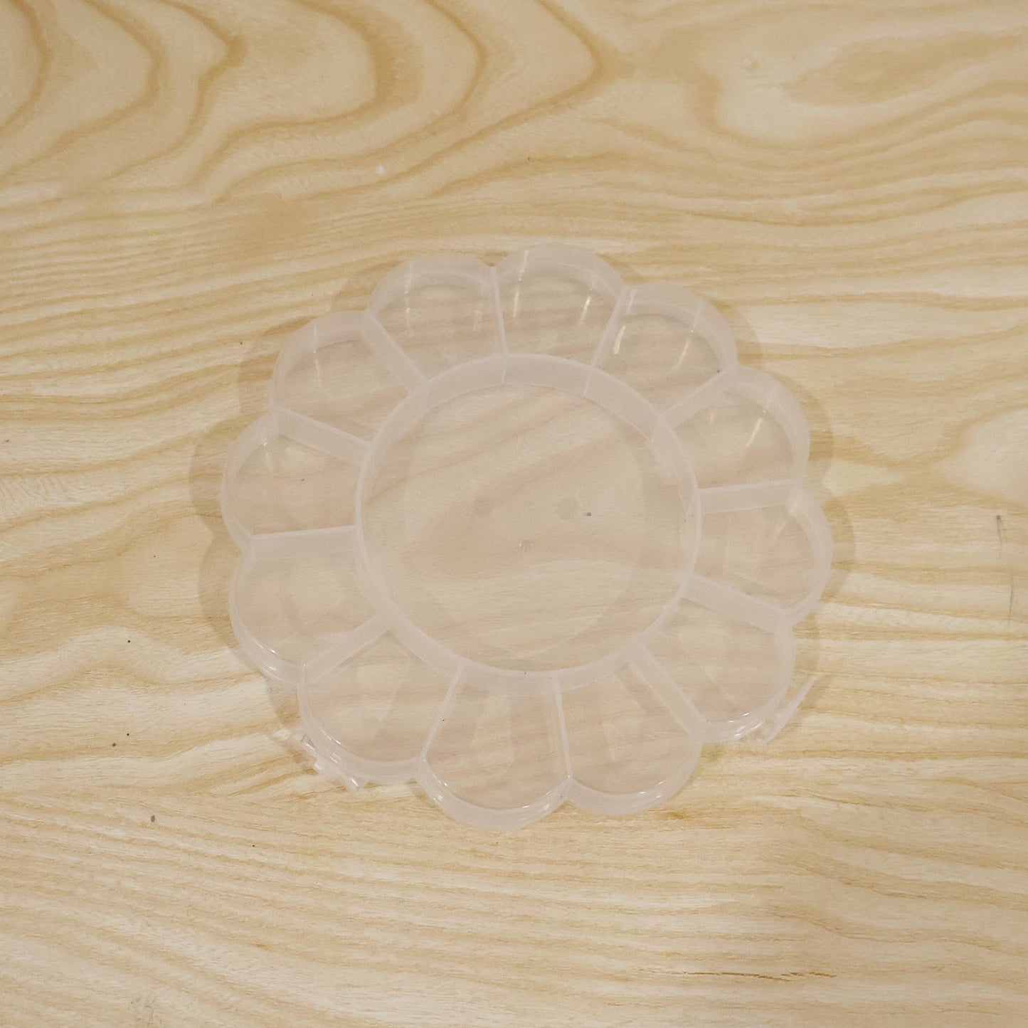 Empty clear flower-shaped plastic organizer box with 13 compartments on a light wood grain surface.