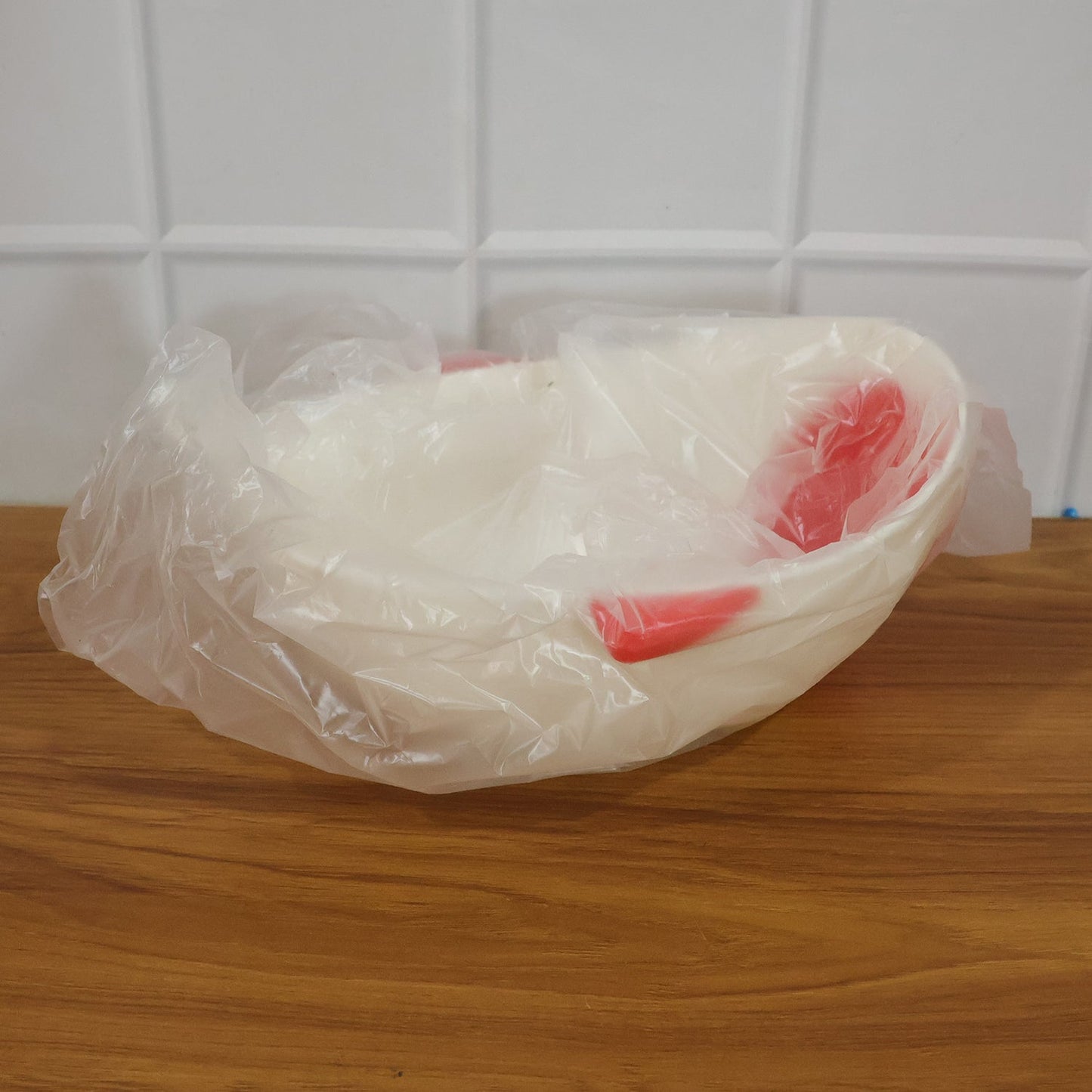A white whale-shaped rice drainer bowl with red accents is wrapped in clear plastic packaging on a wooden surface.