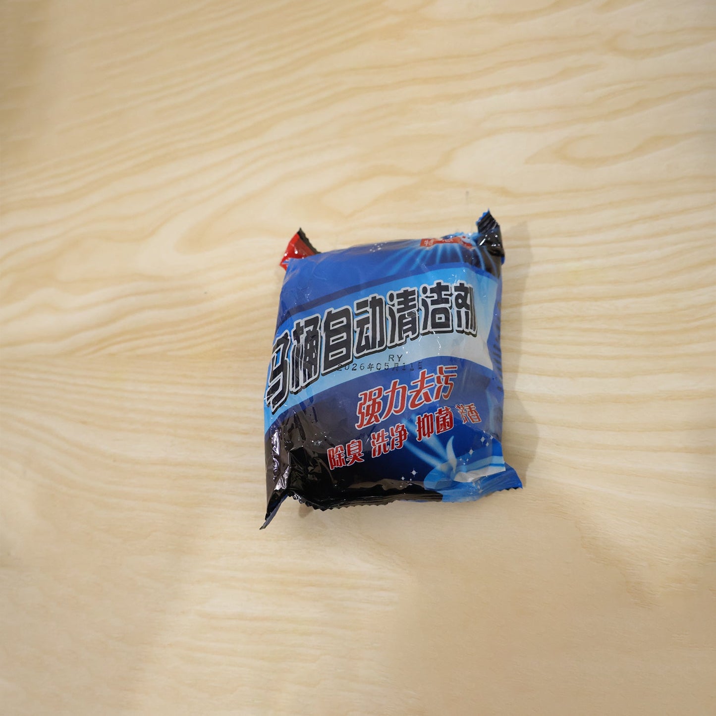 A blue and black package of toilet cleaner tablets with Chinese text is shown on a light wooden surface.
