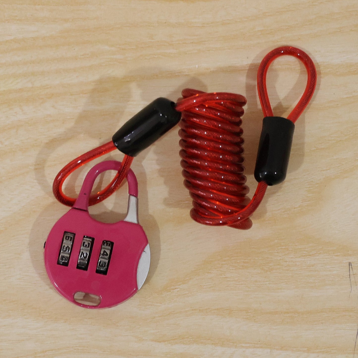 A pink combination lock with a red coiled cable is displayed on a light brown wooden surface.