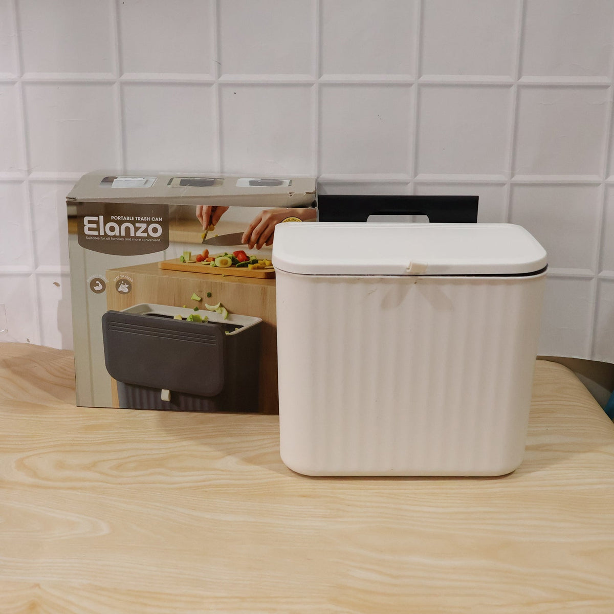 A white ribbed compost bin with a closed lid sits next to its product box on a light wooden surface.