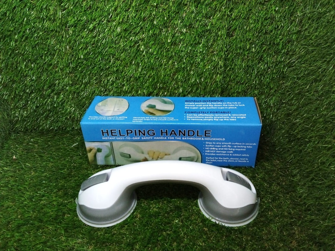 A white and gray suction grip handle and its blue box are placed on a vibrant green artificial grass surface.