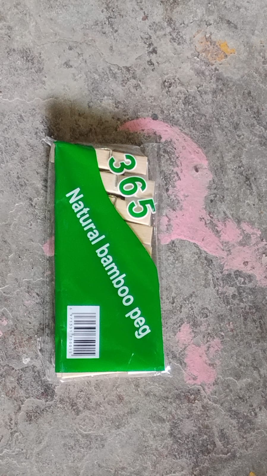 A clear plastic package of natural bamboo pegs with a green label, resting on a concrete surface.