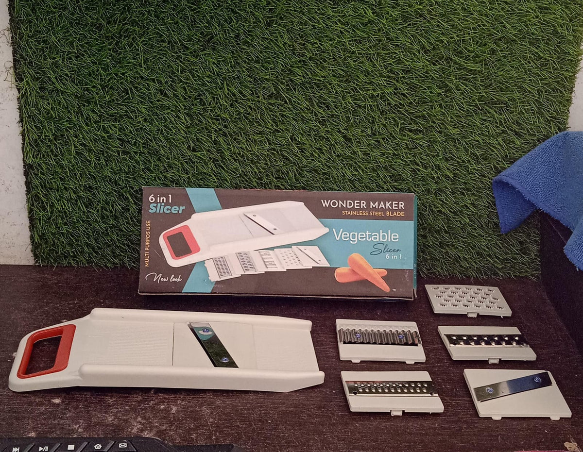 A white and red mandoline slicer, its interchangeable blades, and its product box displayed on a dark surface.