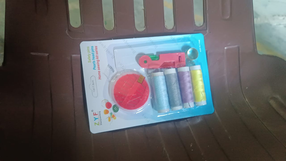 A packaged sewing kit, including thread spools, a needle disc, and a threader, resting on a brown chair.