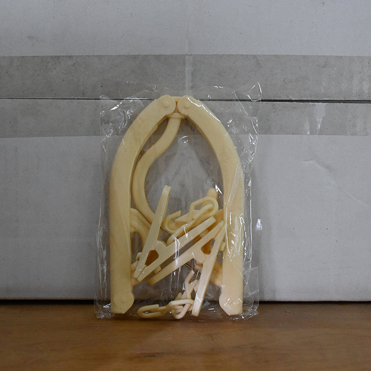 A single beige foldable clothes hanger with clips is sealed in a clear plastic package against a plain background.