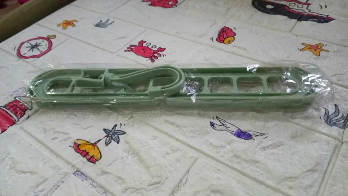 A green plastic multi-hole hanger in clear plastic packaging on a patterned surface.