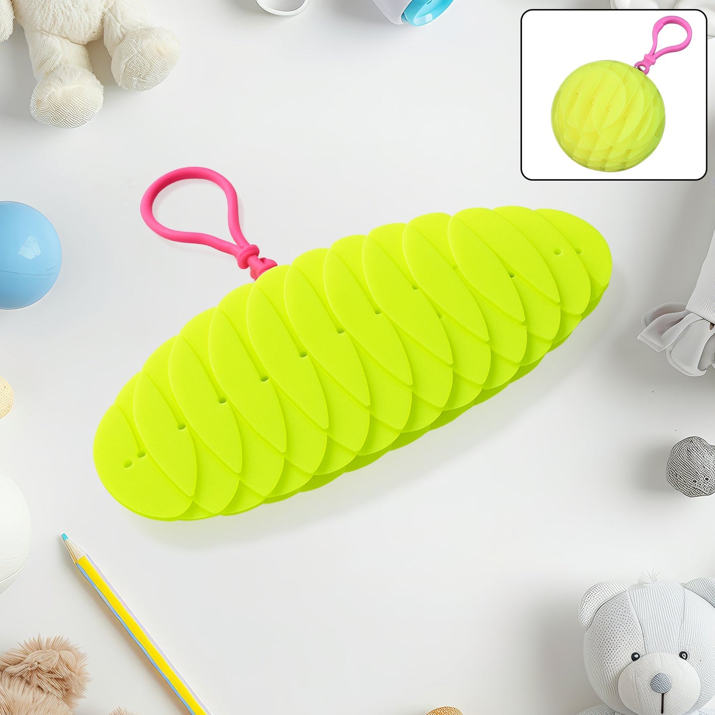 A bright green collapsible silicone ball keychain with a pink loop, shown partially collapsed on a white surface with toys,