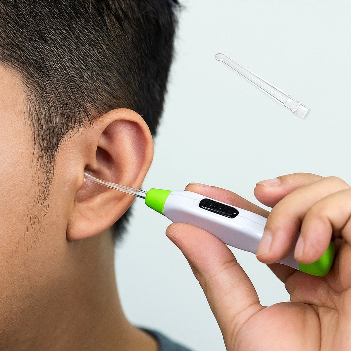 A person holds a white and green LED flashlight earpick with a clear tip to their ear, with an extra tip floating above.