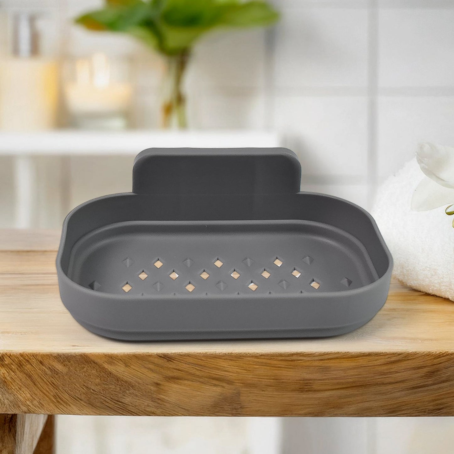 A gray self-adhesive soap dish with drainage holes is displayed on a wooden surface in a bathroom.