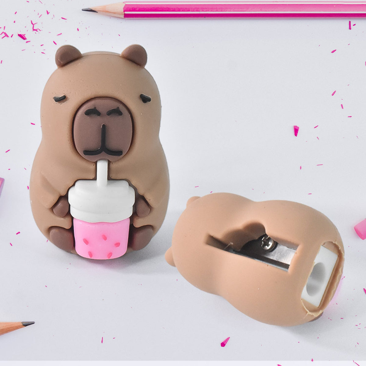 Two capybara pencil sharpeners on a white surface with pink pencil shavings and a pink pencil in the background.