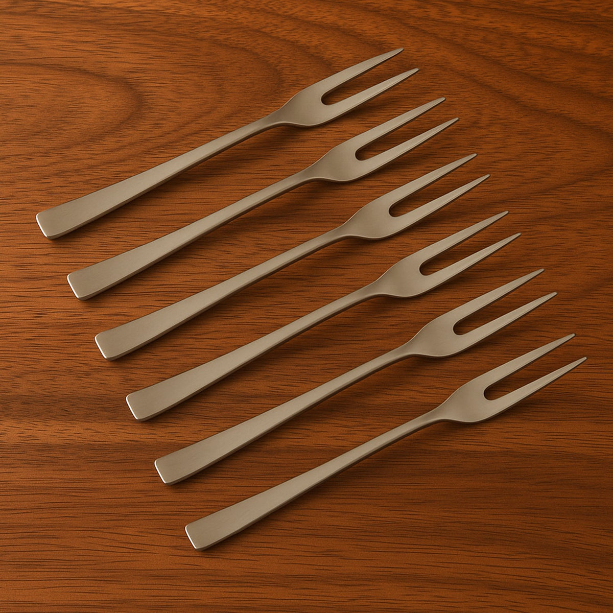 Six silver stainless steel fruit forks neatly arranged in a diagonal pattern on a warm wooden table.