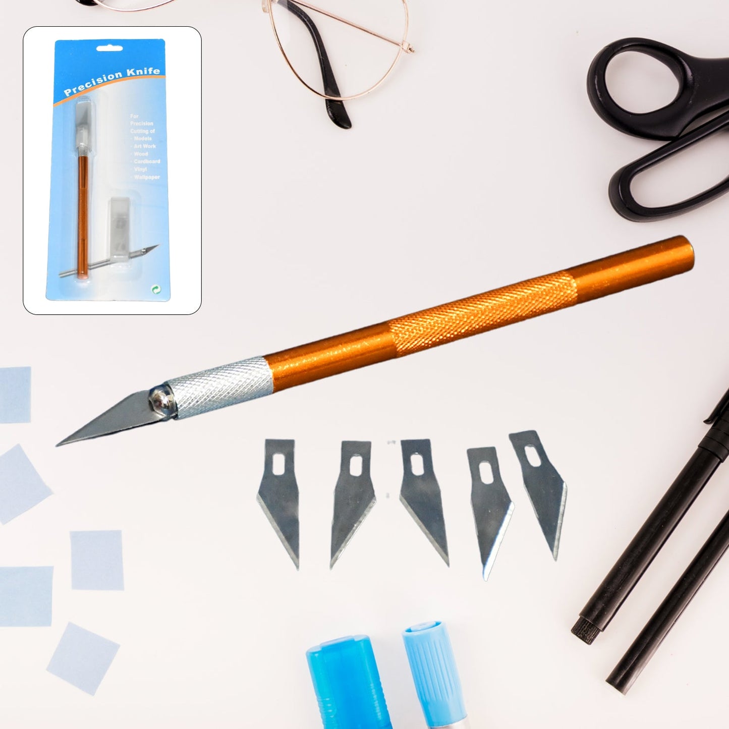 Orange precision knife, five blades, and product packaging on a light desk with glasses and scissors.