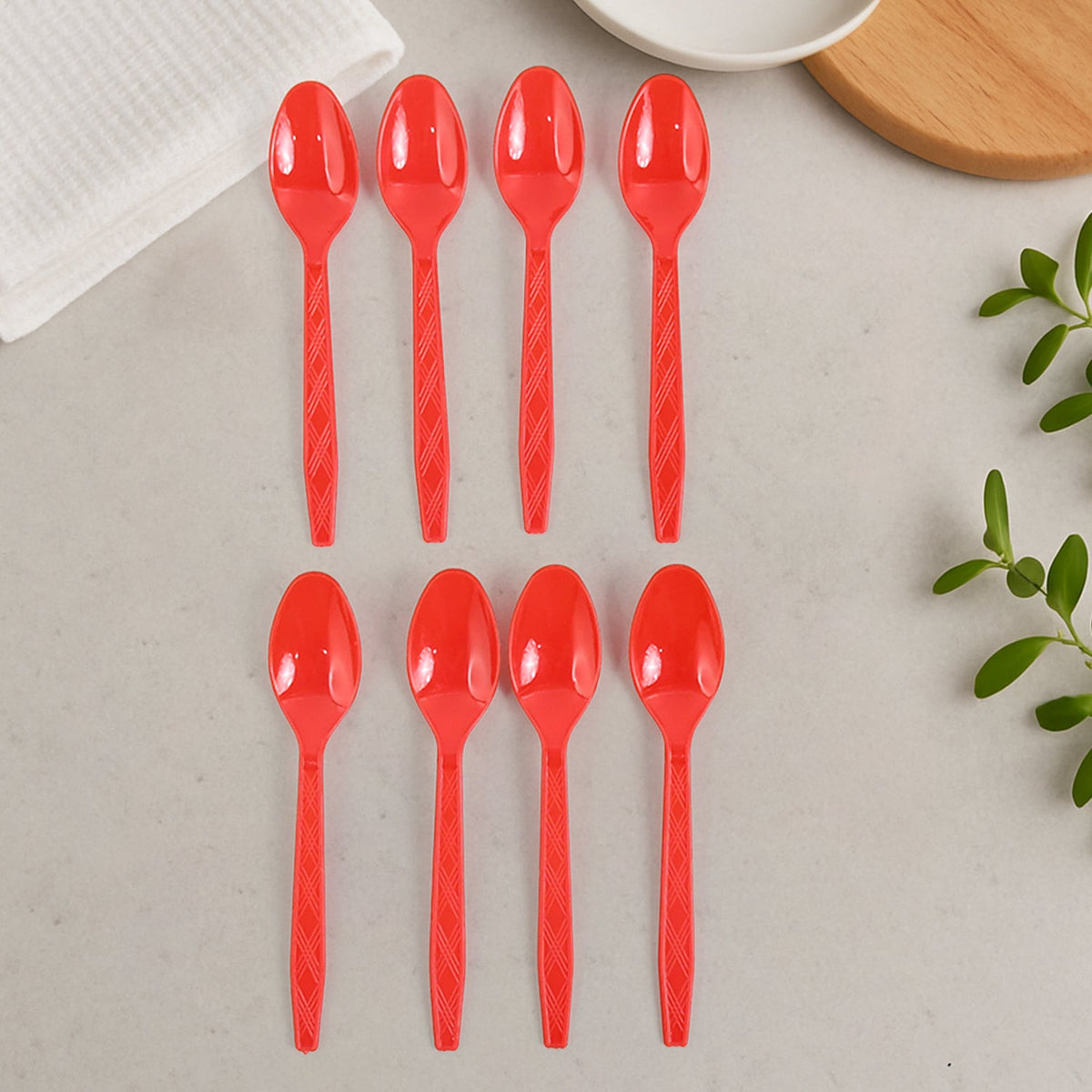 Eight red plastic spoons with textured handles neatly arranged in two rows on a light gray surface.