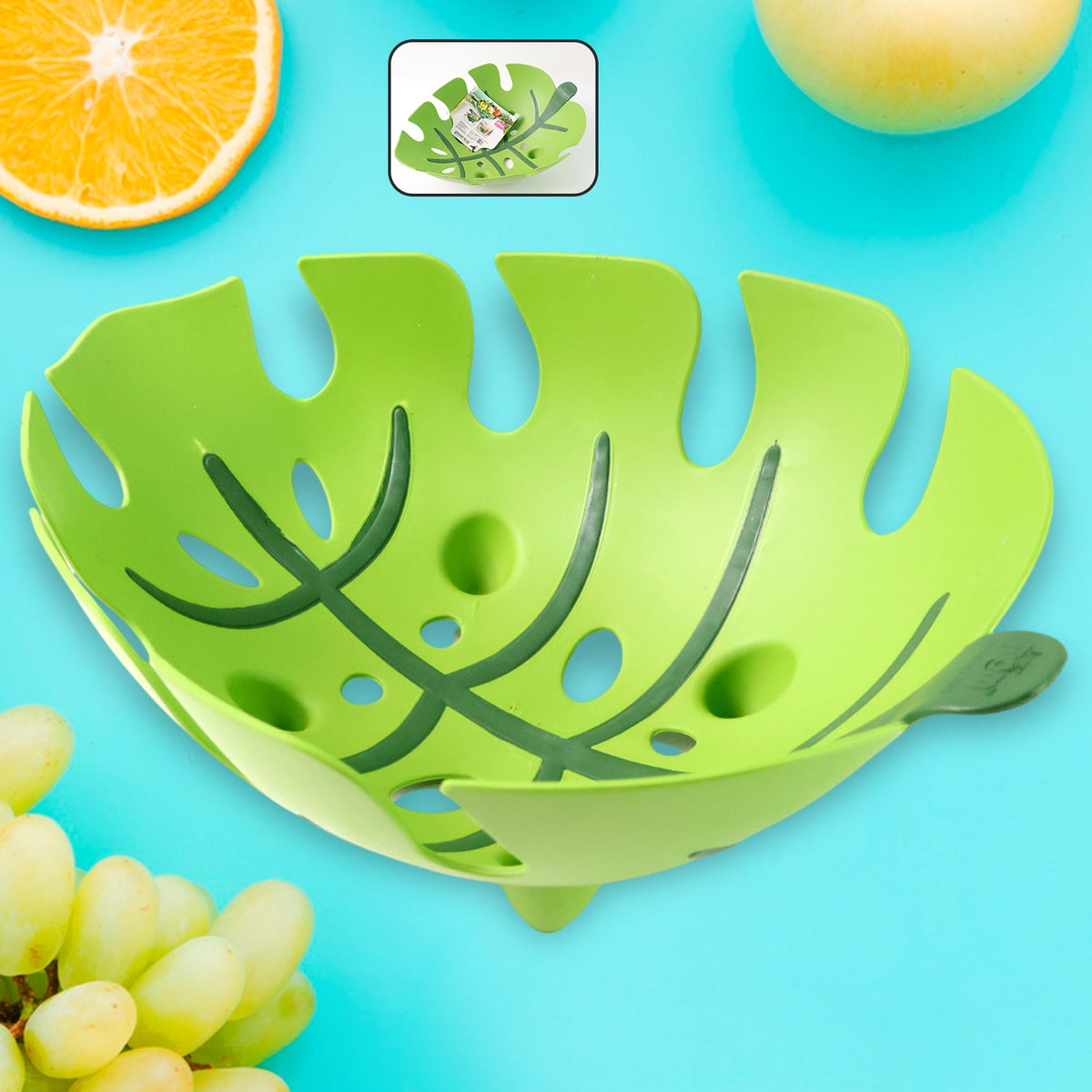 A vibrant green leaf-shaped plastic fruit basket on a bright blue background with fruit slices.