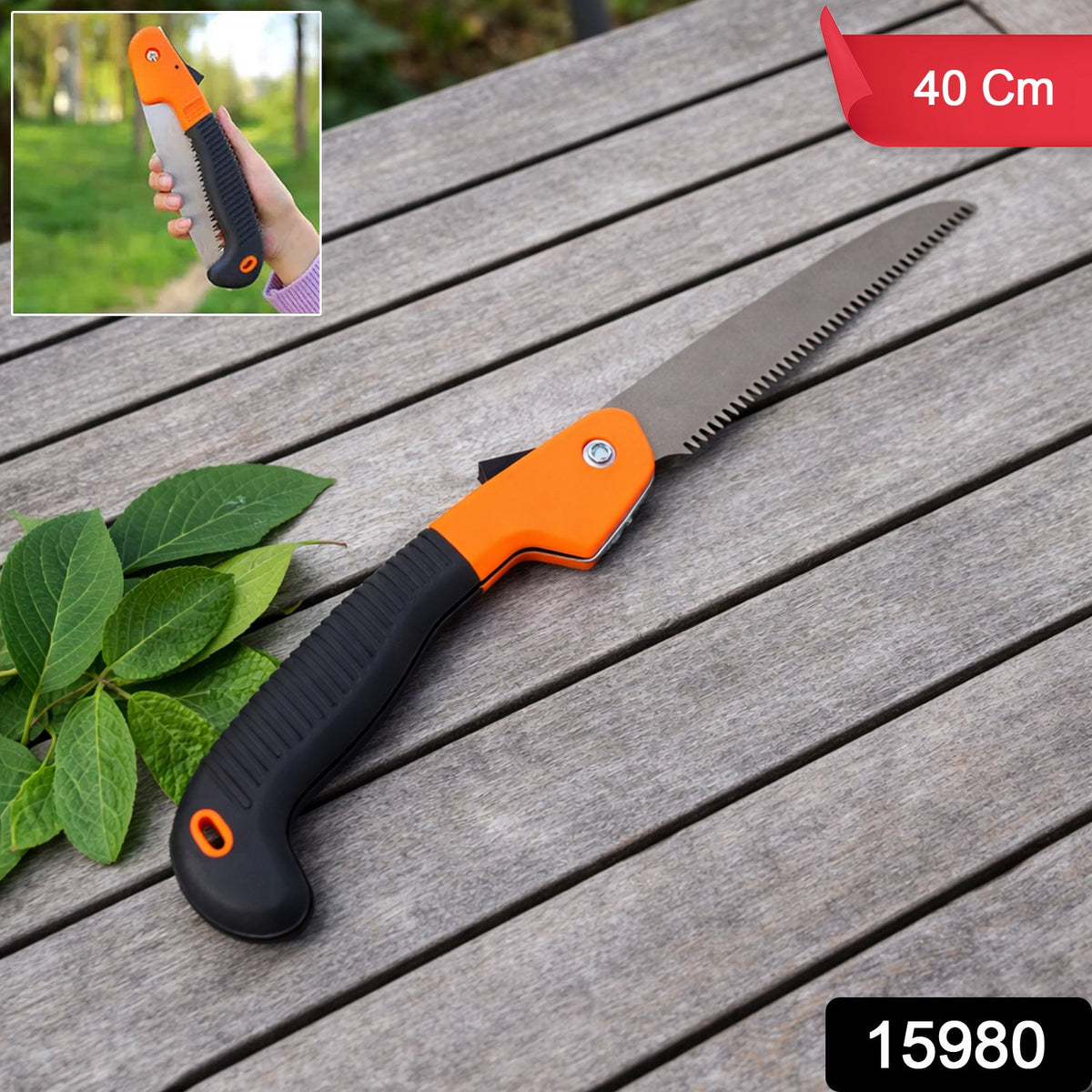 A folding hand saw with an orange and black handle and metal blade lies on a wooden table, with an inset of a hand holding