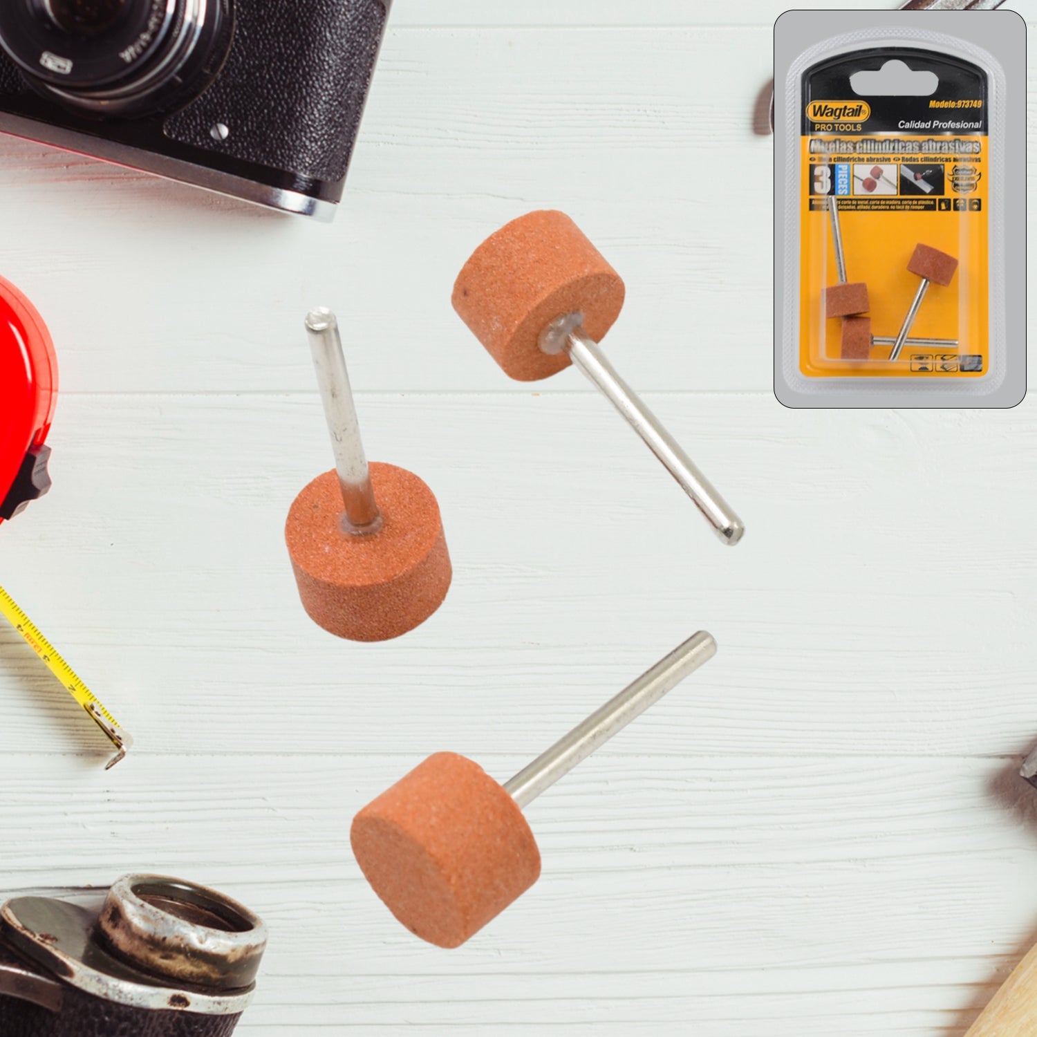 Three cylindrical abrasive grinding wheels with metal shanks on a white wooden surface with tools.