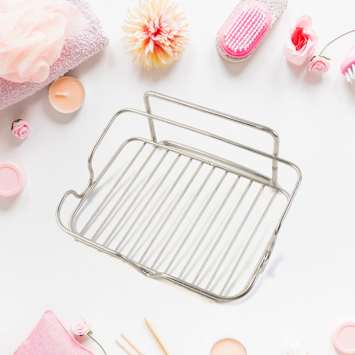 A stainless steel wire soap dish is shown from above, surrounded by pink towels and bath products.