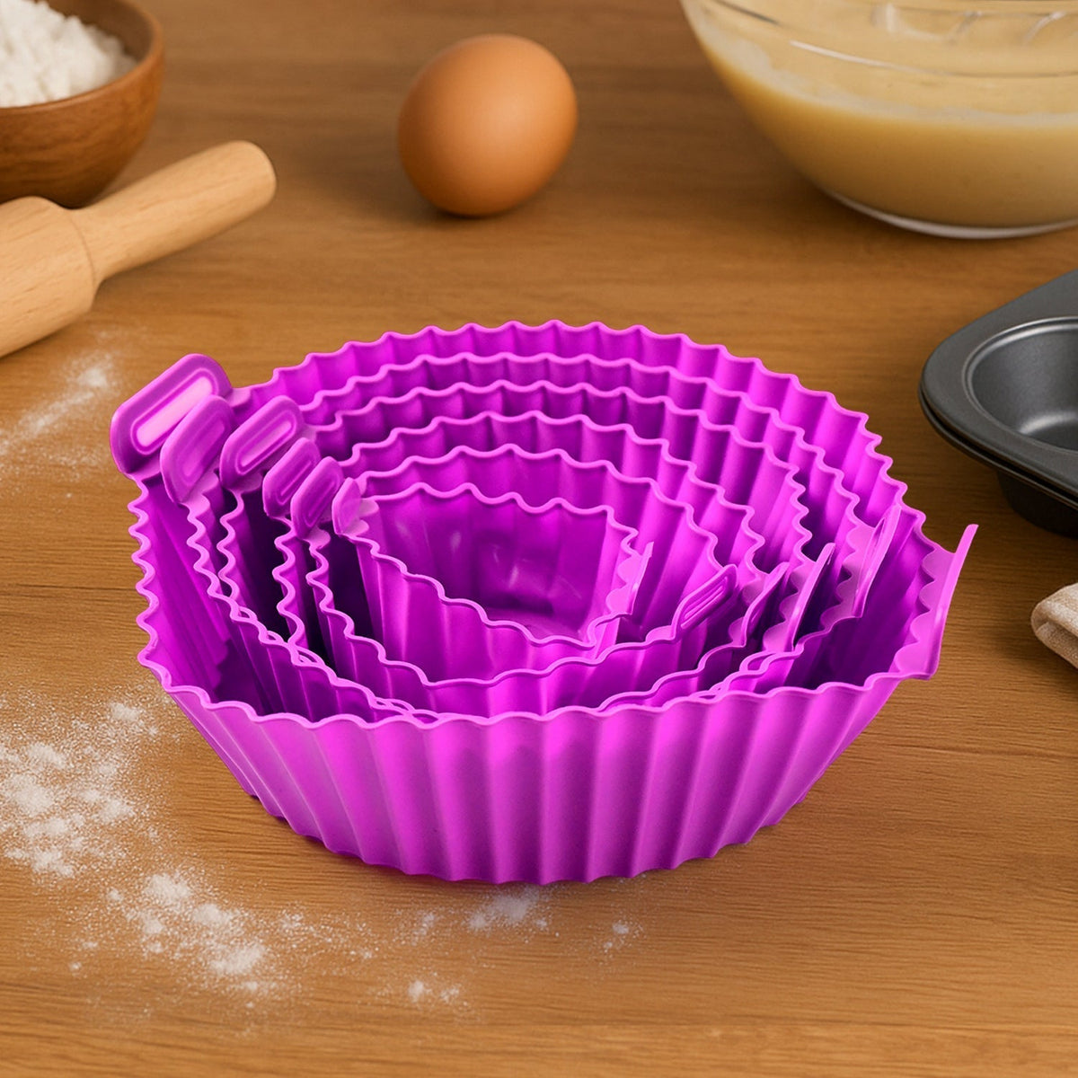 A nested set of purple silicone air fryer pots with handles on a wooden surface with baking ingredients.
